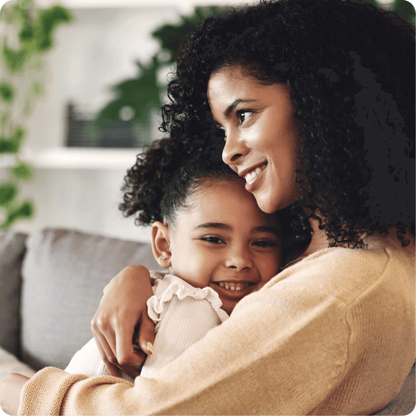 Mãe de cabelos cacheados sorrindo enquanto abraça sua filha pequena, que também sorri, em um ambiente aconchegante.